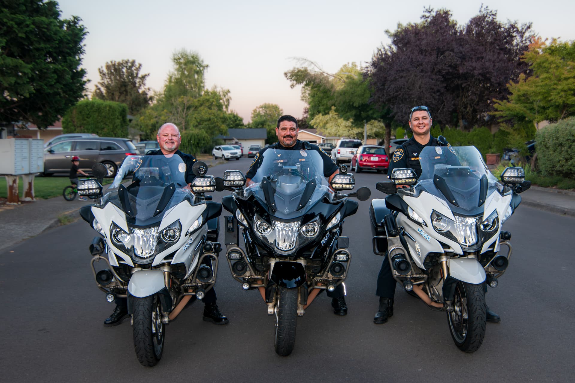 Three Keizer Police Department motorcycle officers on a neighborhood street at sunset.